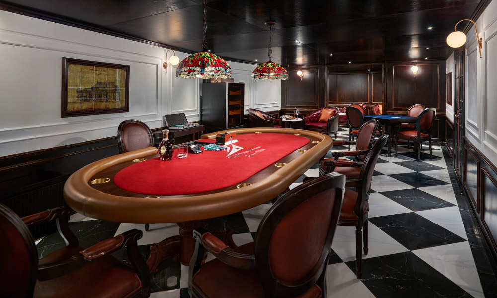 A big poker table with res cover and some games on it, in a room with checkered floor.