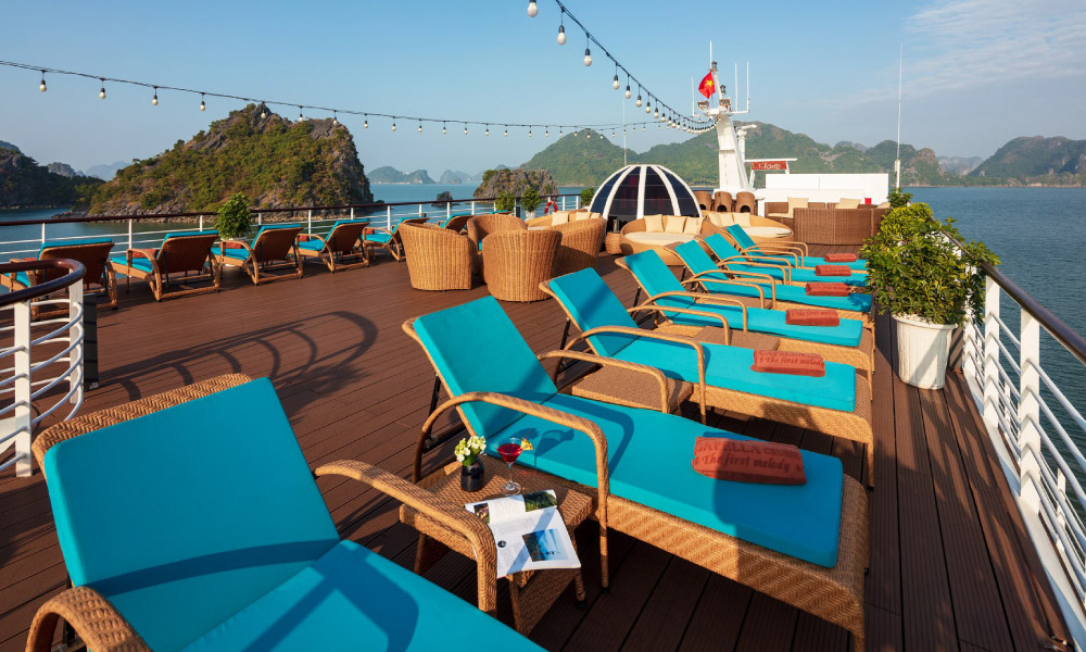 One side of the sundeck on capella cruise with blue lounge chairs and halong islands in the back.