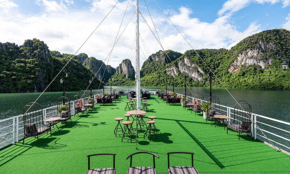 Overview of Carnival sundeck with grass floor and lounge chairs on the sides, facing Halong Bay islands.