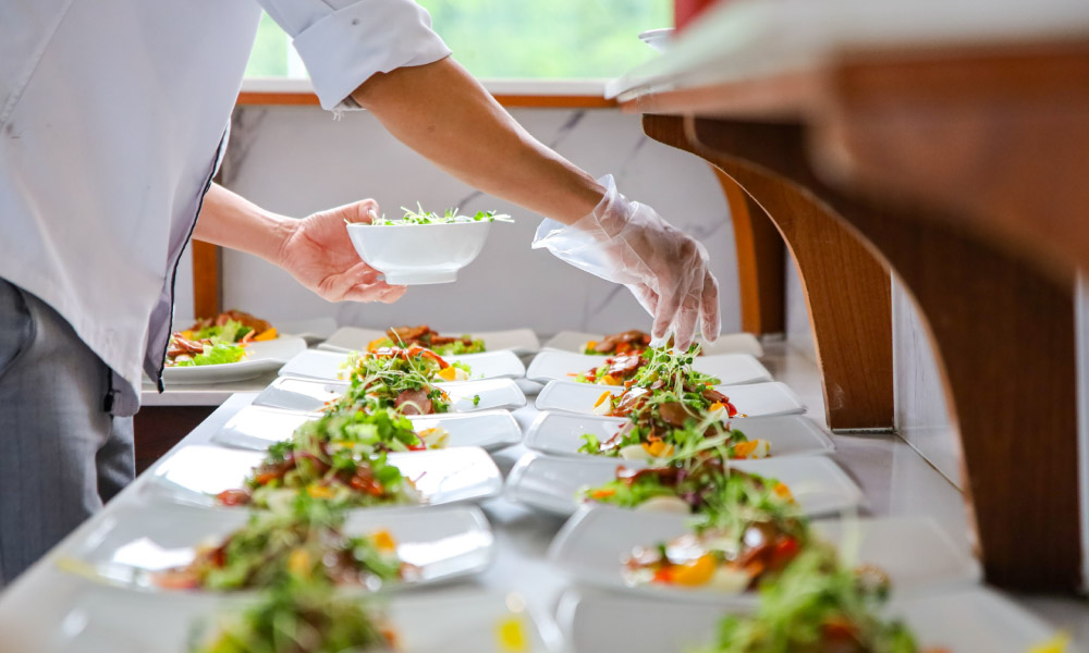 A chef hands putting veggies on plates of seafood dishes.