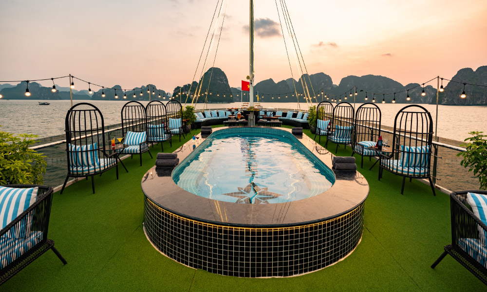 A sundeck with a jacuzzi and blue lounge chairs facing Halong Bay islands.