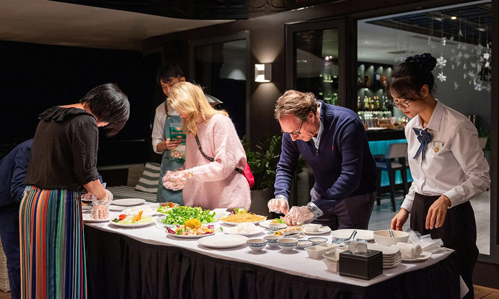 people gathering around a long table and making food