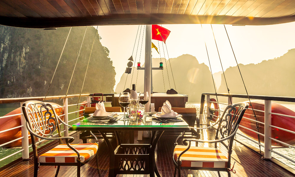 Sunset view in Halong Bay over the sundeck with a table and chairs.