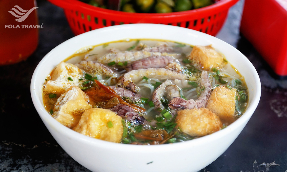 A bowl of noodles with tofu cubes and seafood.