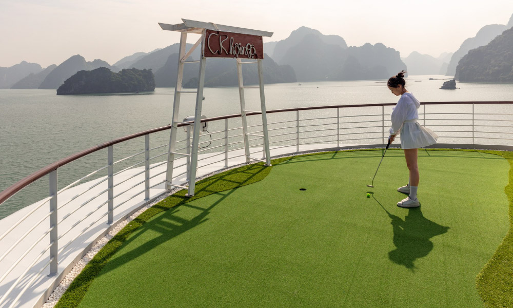 A girl playing golf on the deck of Capella cruise looking out to Ha Long Bay.