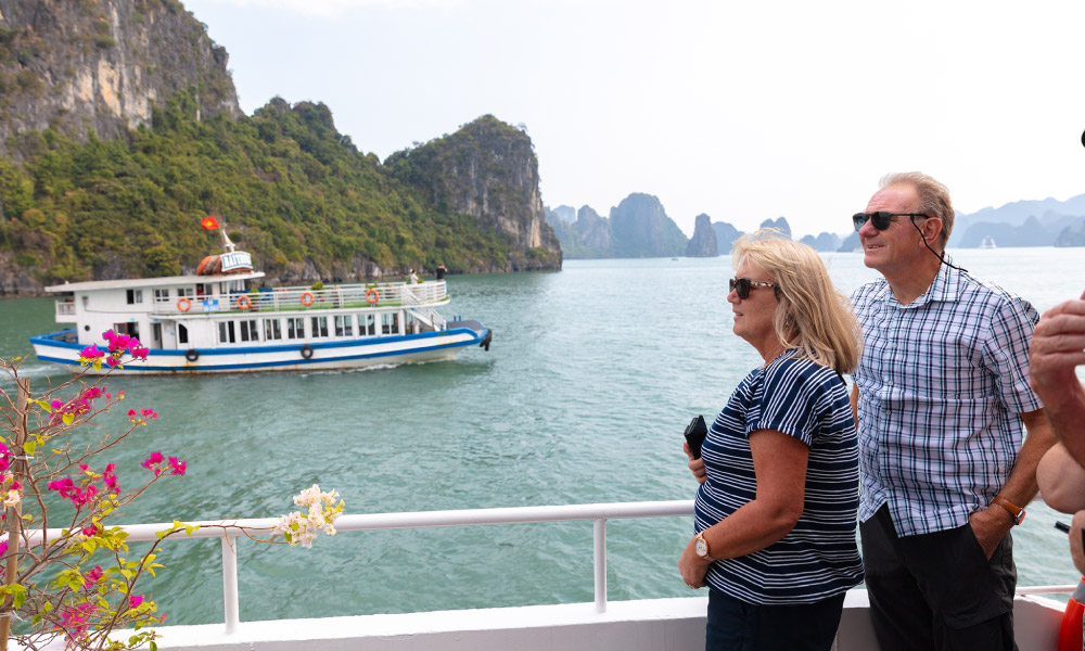 A couple standing on a deck looking at a Halong island and cruise.