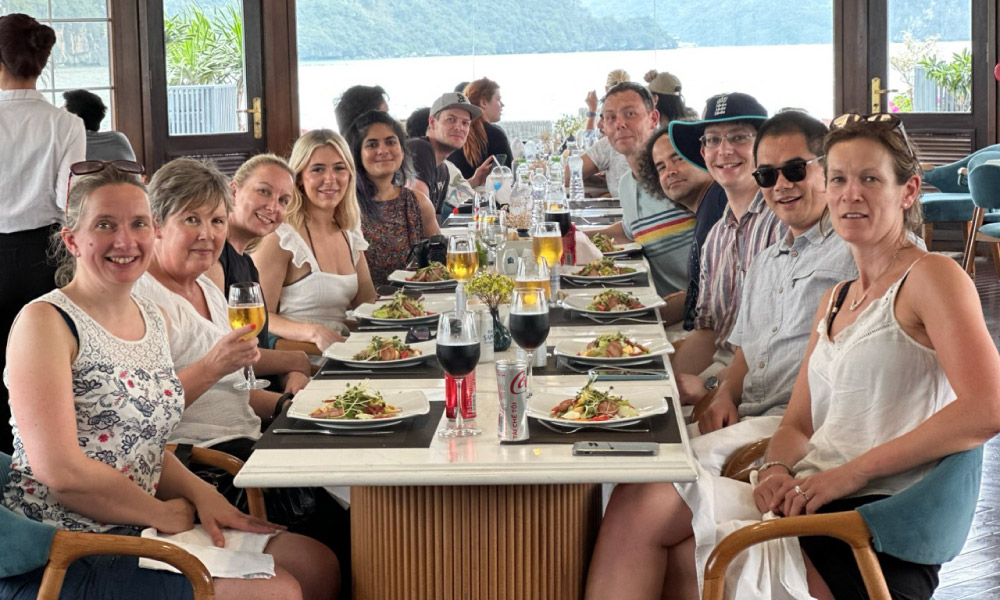 A table in Halong Catamaran Restaurant full of guests with dishes in front of them.