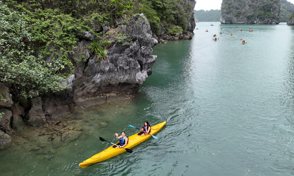 A yellow kayak sailing past Halong Bay islands with a few more in the far.