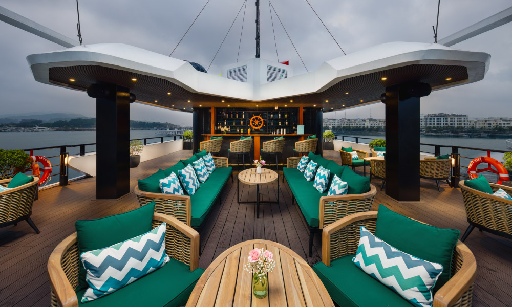 The deck on Halong Catamaran Cruise with wooden chairs, green pillows, and oval wooden tables.