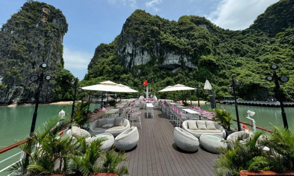 A sundeck with white tables and umbrellas with Halong Bay islands surrounding the cruise.