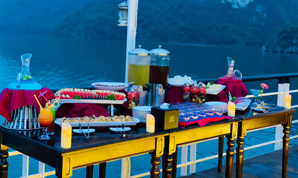 A table with fruits, cakes, and tea bottle for the sunset party.