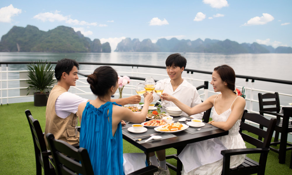 four people eating on the deck of la muse day cruise with open view of halong bay