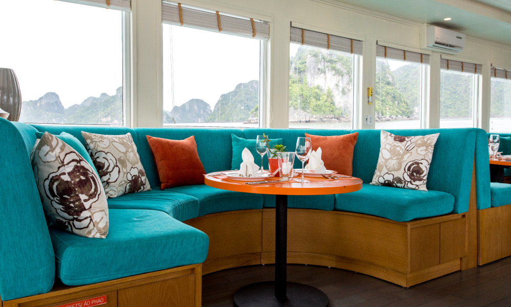 A turquoise lounge chair with orange and flower throw pillows.