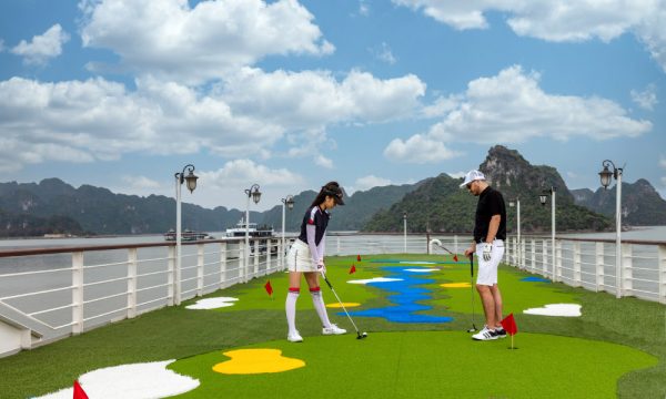 The golf court on the deck of mon cheri cruises with two people playing and halong islands in the background.