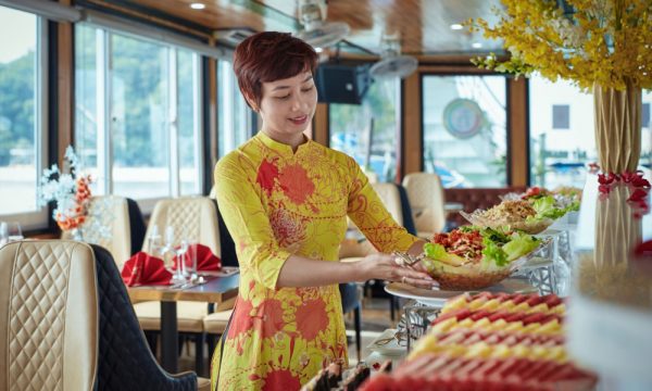 A woman preparing food on a restaurant wearing yellow ao dai.