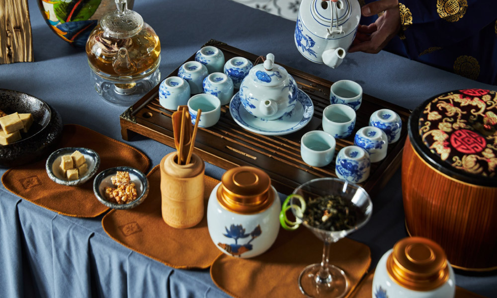 Many Vietnamese teapots and tea cups on a table with blue cover.