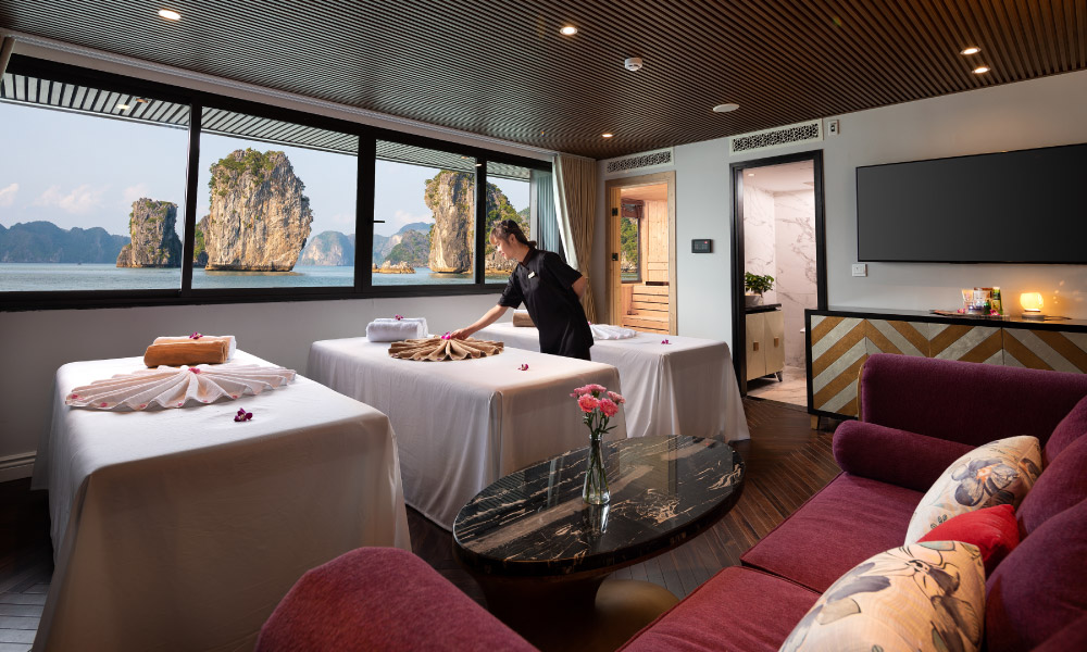 the spa room with 3 beds under a big window looking out to halong islands, a sofa and a oval coffee table