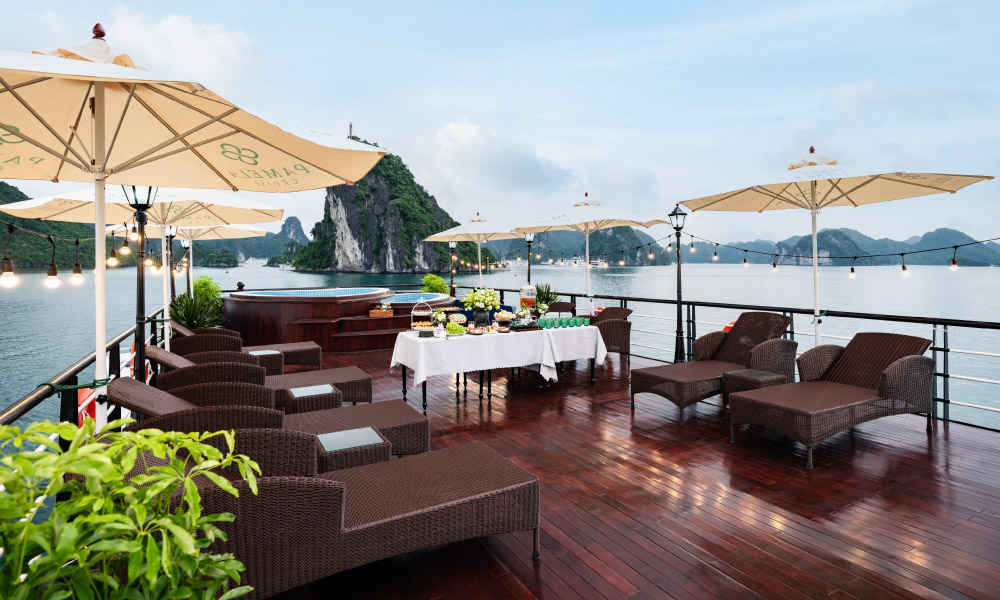 A sundeck with lounge chairs and umbrellas, with open view of Halong Bay sea and islands.