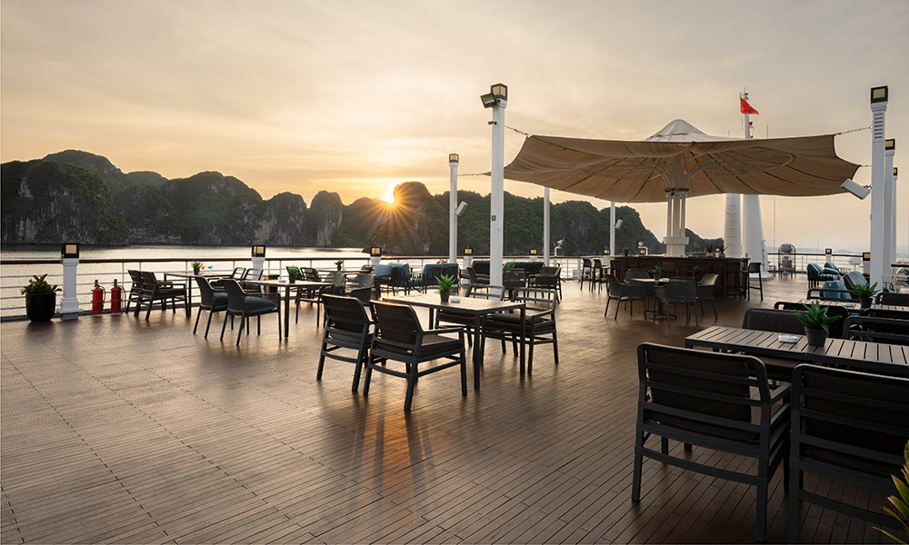 A sundeck with many chairs and a big umbrella, looking out to Halong Bay islands during sunset.