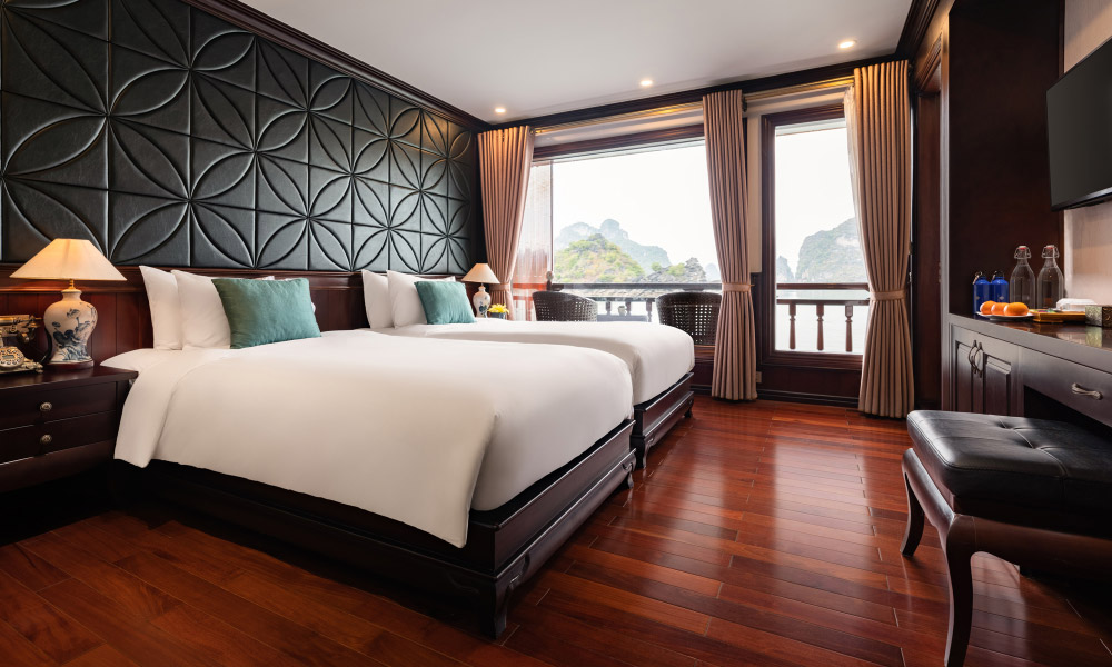 A room with two twin beds on the left facing the TV, with dark wood cabinets, floor, and headboard.