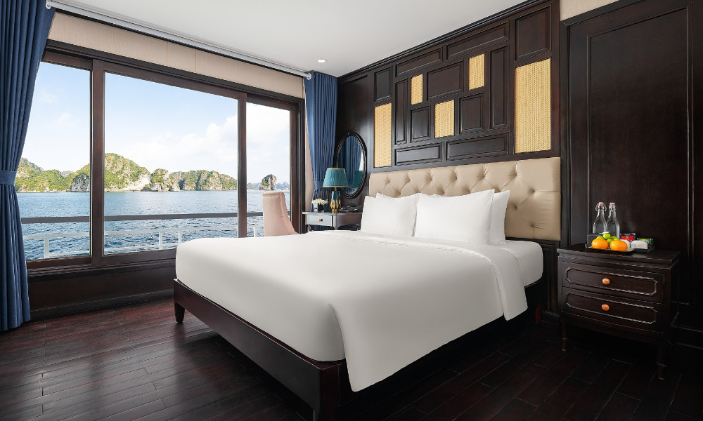 A room with double bed in the middle, a wooden headboard above, next to a big window with view of Halong islands outside.