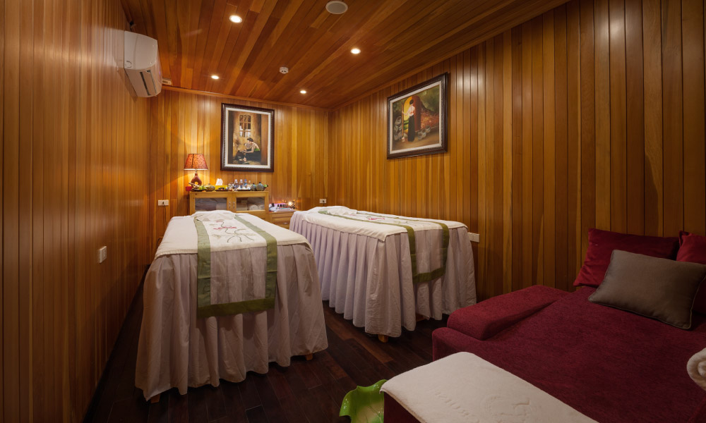 A small wooden spa room with two beds and a red sofa in the corner.