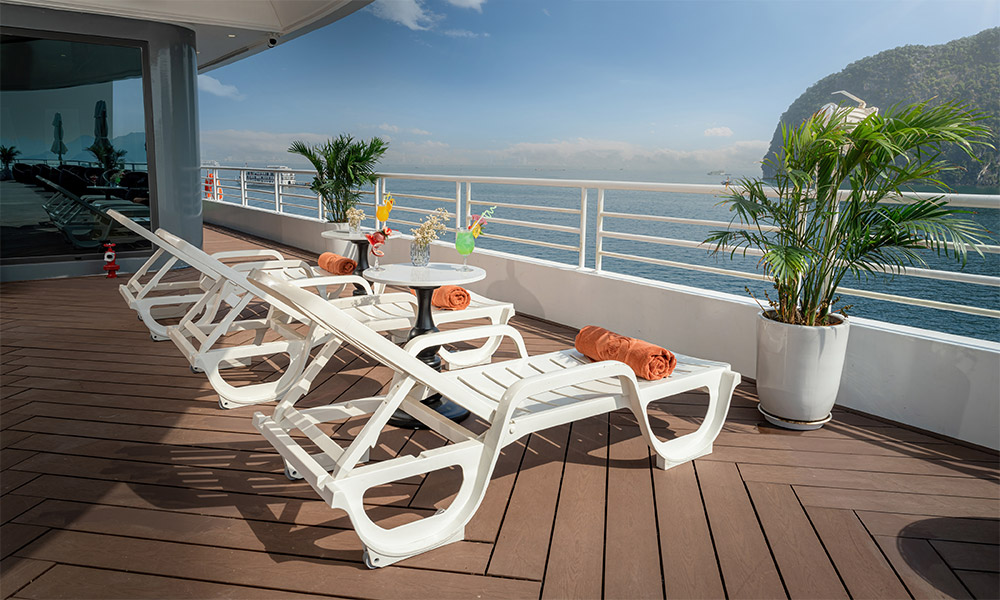 A corner of a sundeck on a cruise with three white sun chairs.