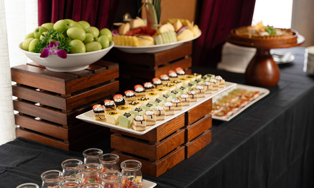 A buffet station with a big tray of cakes and other fruits.