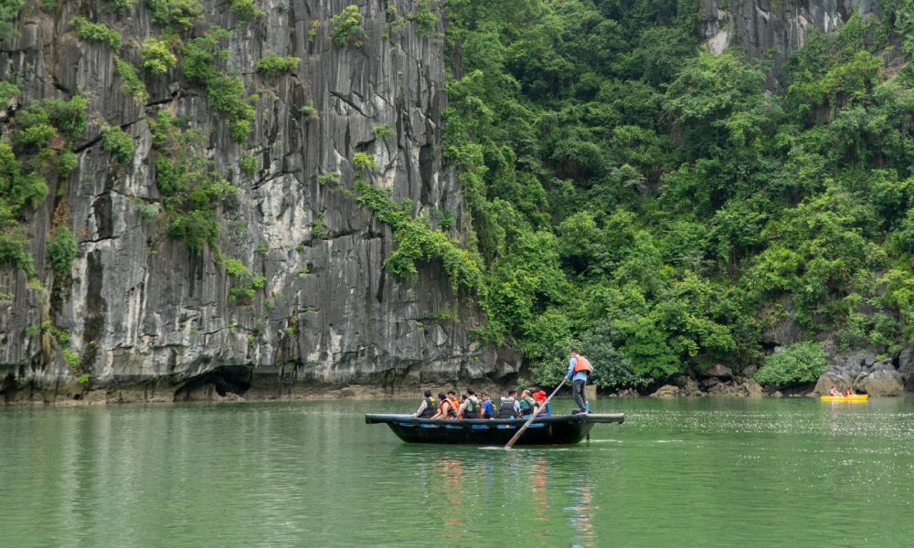 a person rowing a bamboo boat with guests in halong bay