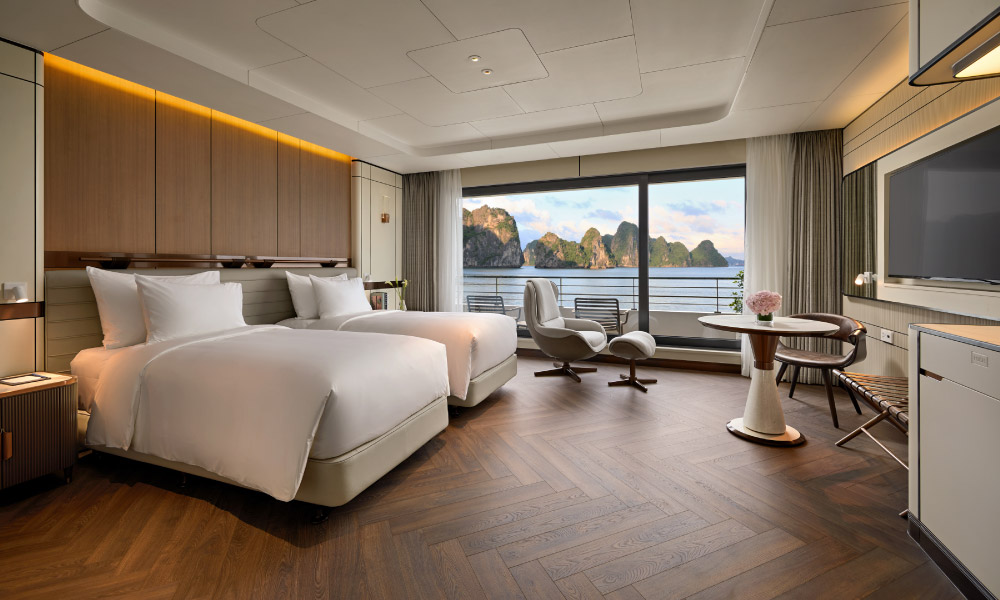 A modern room with two twin beds on the left, a big window with view of Halong Bay, facing a TV and a table.