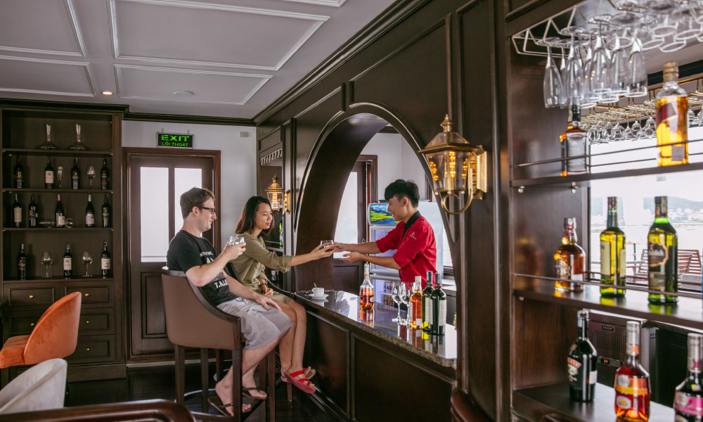 Two guests at a bar and a server handing them drinks.