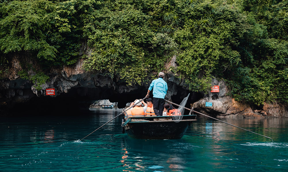 A person rowing a bamboo boat with guests on, going through the Dark & Light Cave.