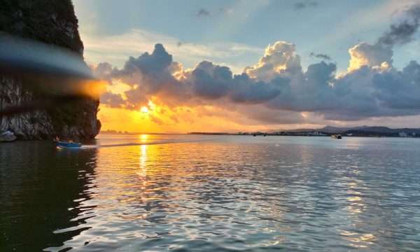 Halong Bay sunset with blue clouds, an island on the left and some small boats.