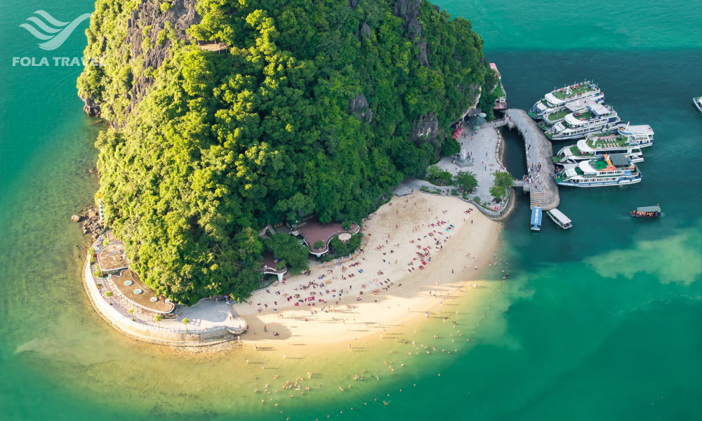 An island looking from top down with a coast and many people on the beach.