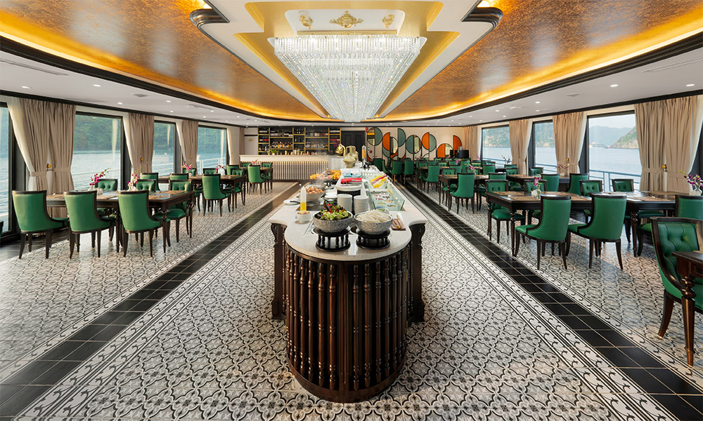 A restaurant with a buffet station in the middle and tables with green chairs on two sides.