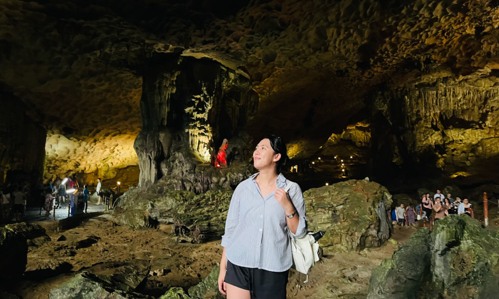 A girl standing in Sung Sot Cave with some other guests walking behind.