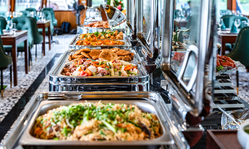 A buffet station with many trays of Vietnamese food in the restaurant of Hercules Luxury Cruise.