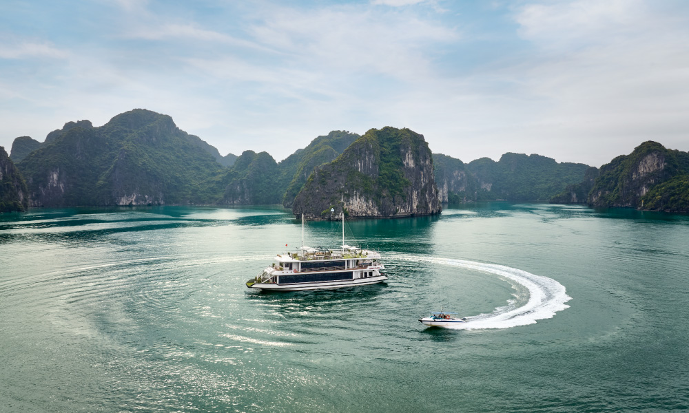 Hercules Premium Cruise in the middle of Halong Bay with a small boat making a round foam around it.