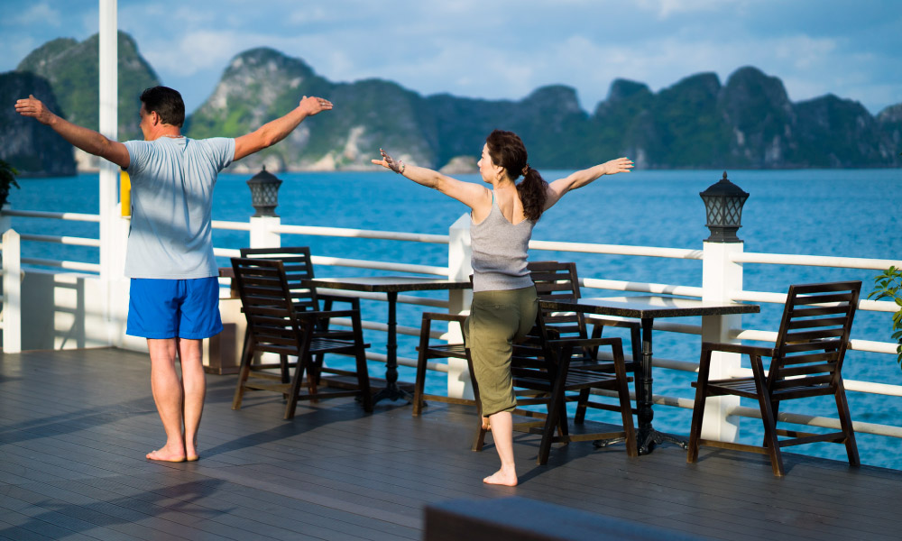 Two people doing exercise on a cruise with Halong Bay island in the back.