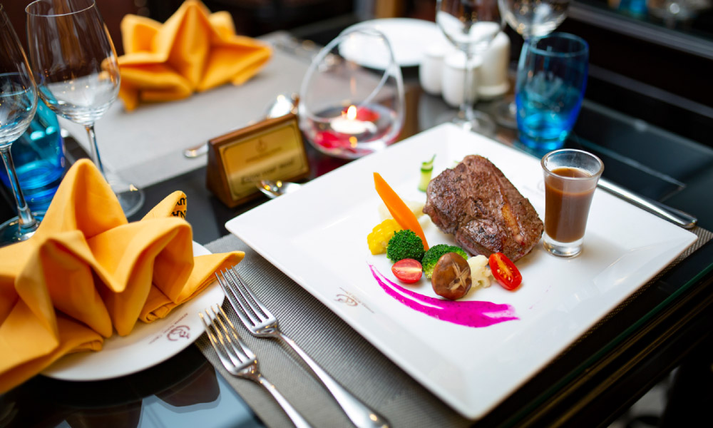 A plate of gourmet steak on a table with forks and napkins.