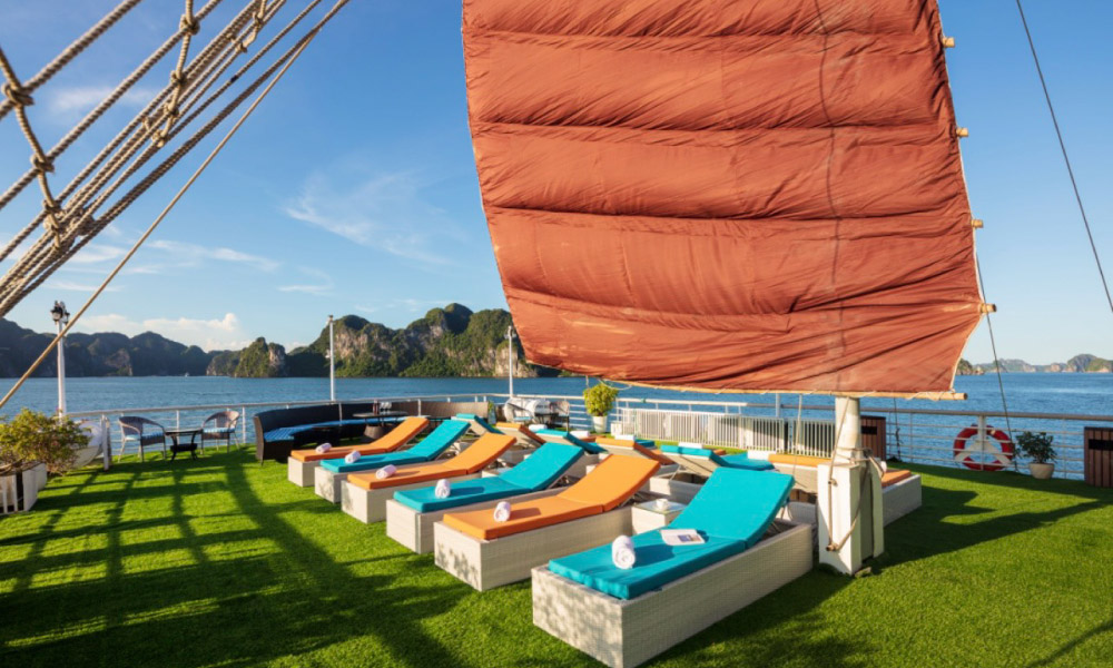 A sundeck with a row of turquoise and orange chairs under a big sail.