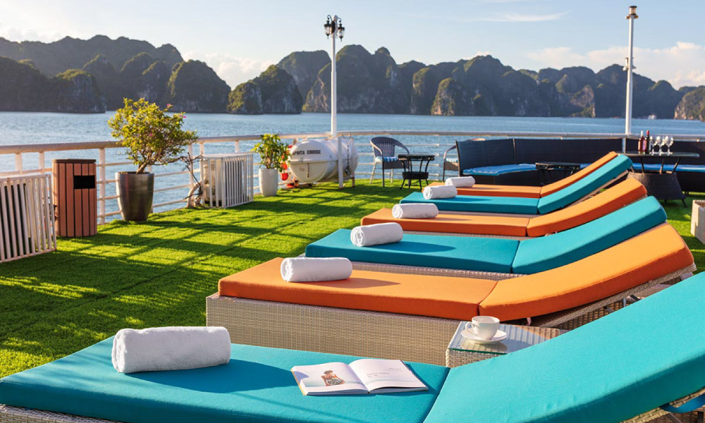 A row of orange and turquoise sun chairs on a cruise with view of Halong Bay islands.