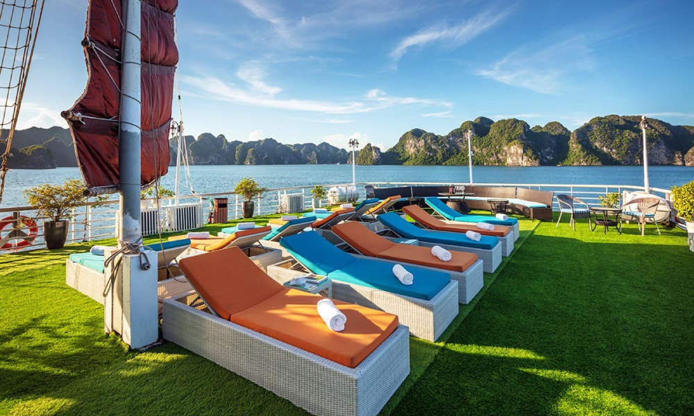 Halong Bay sea and islands looking from the sundeck of a cruise with lounge chairs.