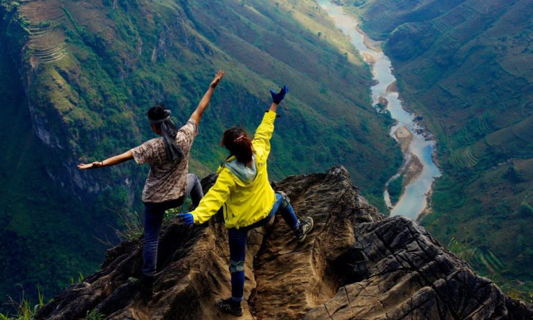 Two people dancing on a rock looking down to nho que river.