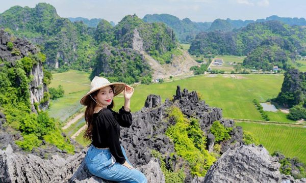 A girl sitting on Hang Mua peak with view of Tam Coc behind.