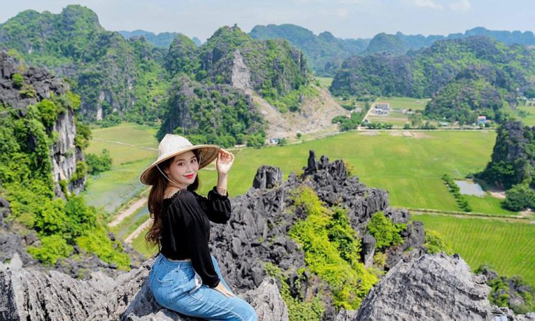 A girl sitting on Hang Mua peak with view of Tam Coc behind.