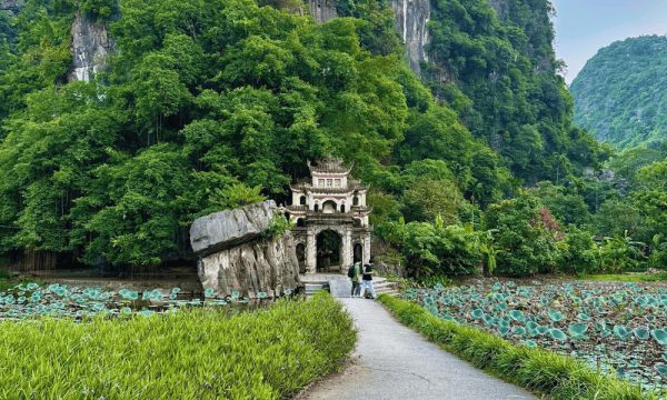 A road in the middle of lotus lake running to the gate of Bich Dong Pagoda in front of a mountain.