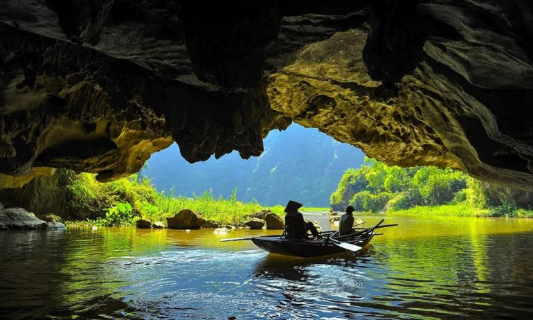 A boat under a limestone islands on the water with outside view of green trees.