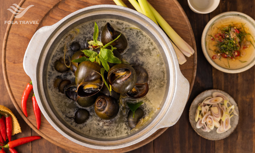 A pot of boild snails and some sauces, garlic and chilli on the side.