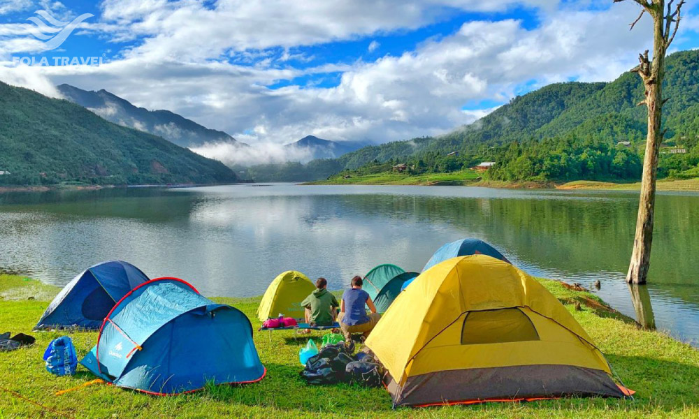 Two people among colorful camps in front of a lake.